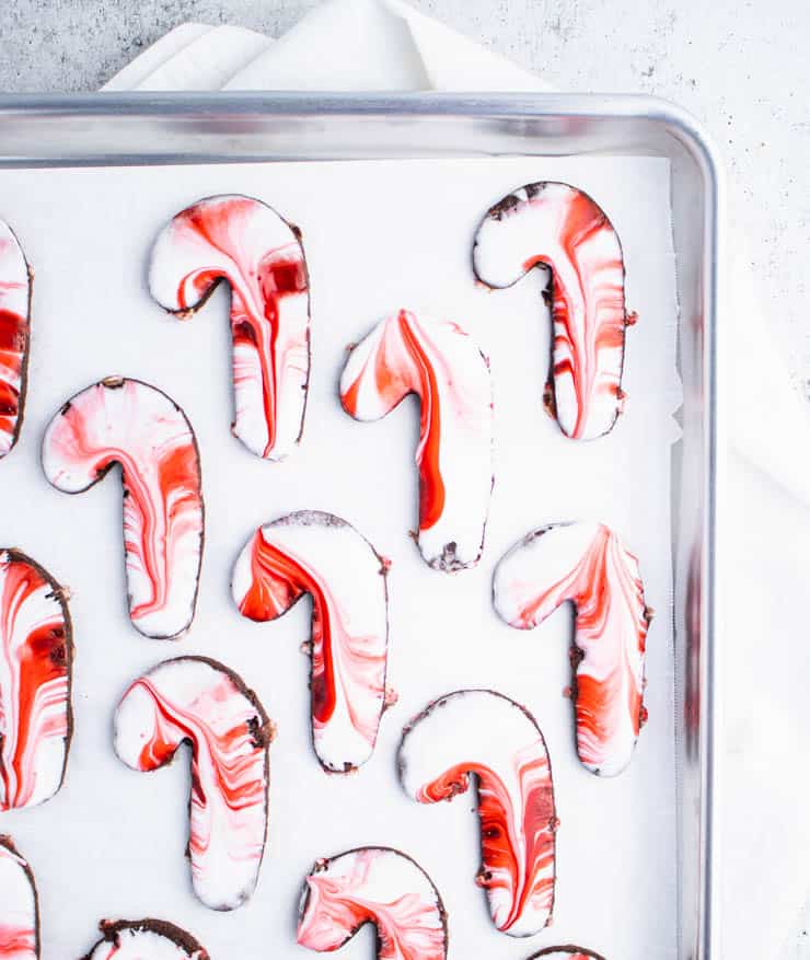 White and red icing swirled candy cane shaped sugar cookies on a parchment paper lined silver baking sheet.