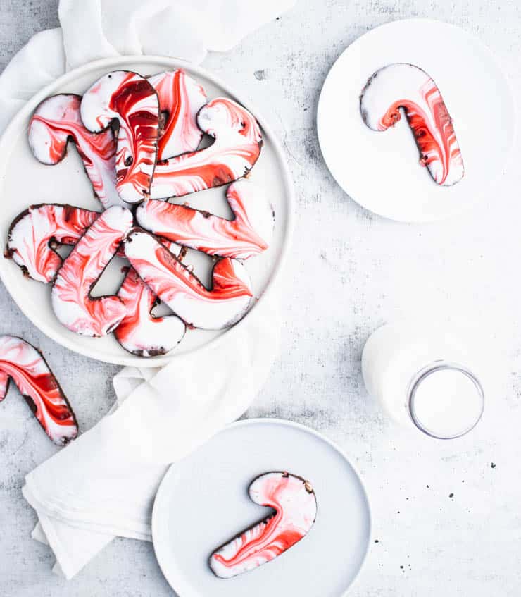Overhead view of a plate of chocolate peppermint candy cane shaped sugar cookies with plated cookies around it.