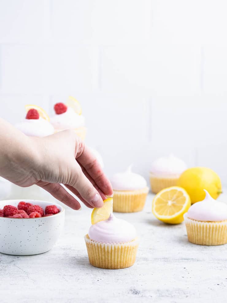 Hand placing a lemon wedge on top of a pink frosted cupcake.