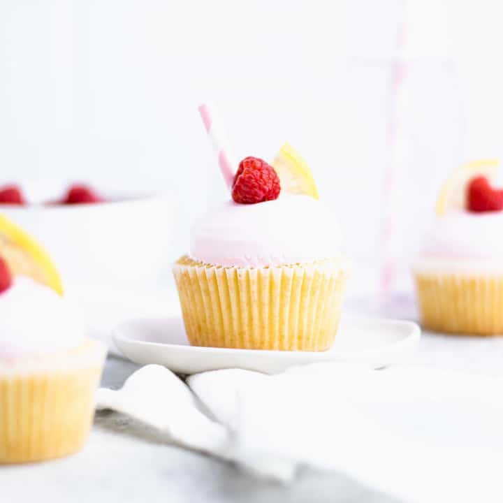 Close up of raspberry lemon cupcake on a plate with out of focus cupcakes around it.
