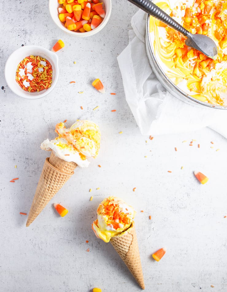 overhead shot of two cones of candy corn ice cream laid on a off-white backdrop