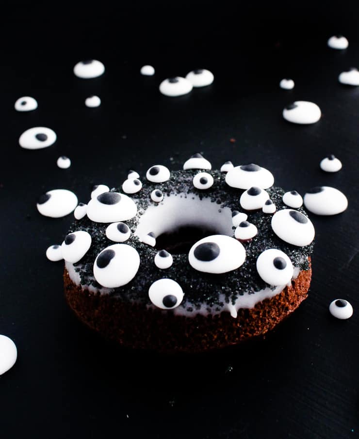 doughnut with royal icing eyes shot from the side against a black backdrop