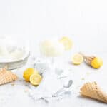 lemon sorbet in a glass with ice cream cones and lemons in the background.