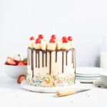 frosted banana split cake in front of a stack of plates and a bowl of strawberries