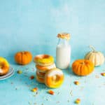 a stack of candy corn doughnuts in front of a jug of milk with doughnuts and pumpkins in the background
