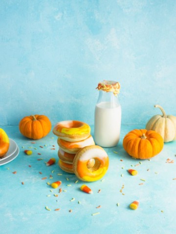 a stack of candy corn doughnuts in front of a jug of milk with doughnuts and pumpkins in the background