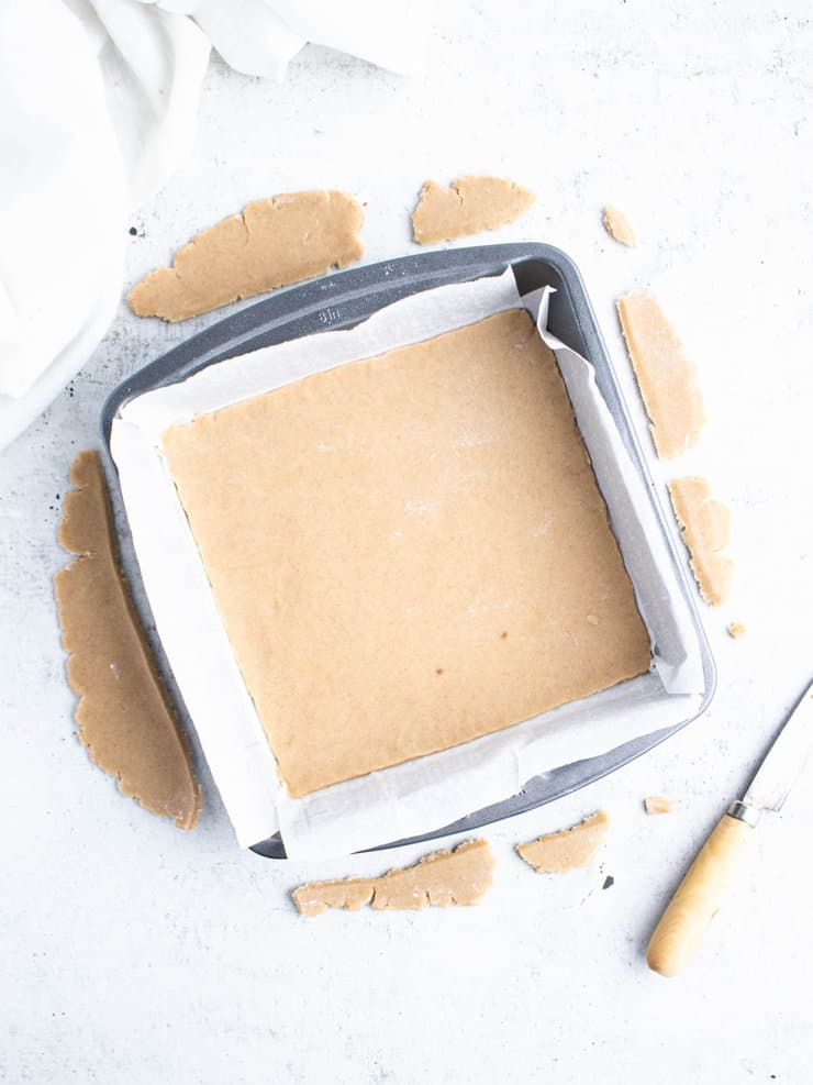 Graham cracker dough in a square, silver pan with trimmed pieces around the sides.