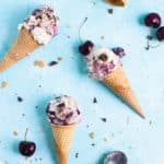 Three ice cream cones with cherries and chunks of chocolate scattered about
