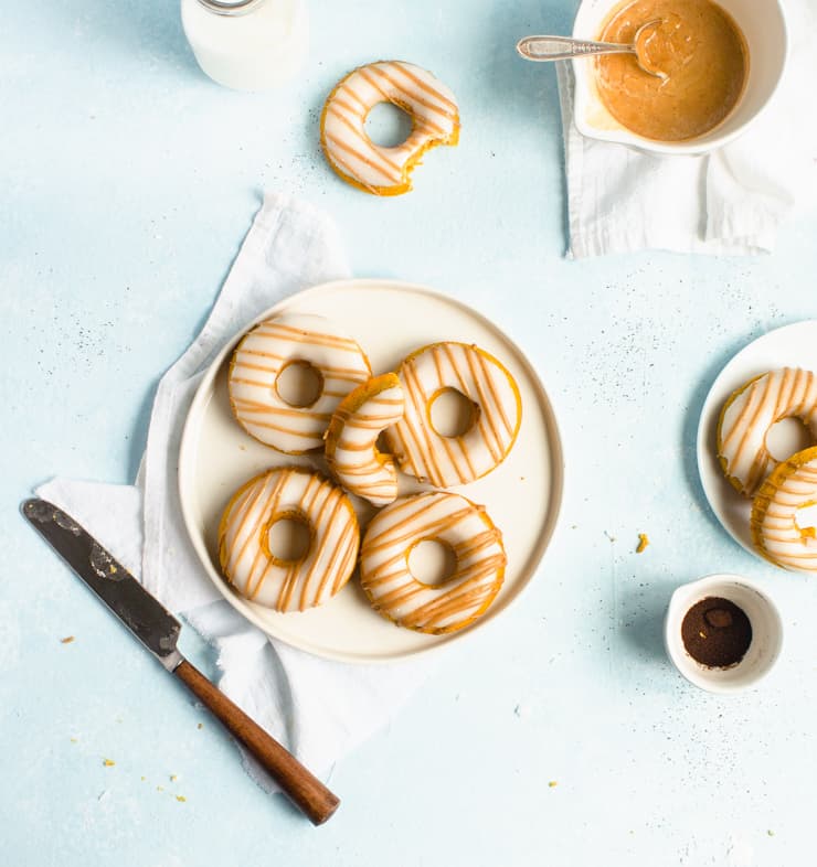 Plate of doughnuts on a white napkin with a knife, jar of milk and bowl of glaze around it