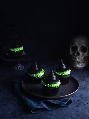 three witch hat cupcakes on a plate with a skull and another cupcake in the background
