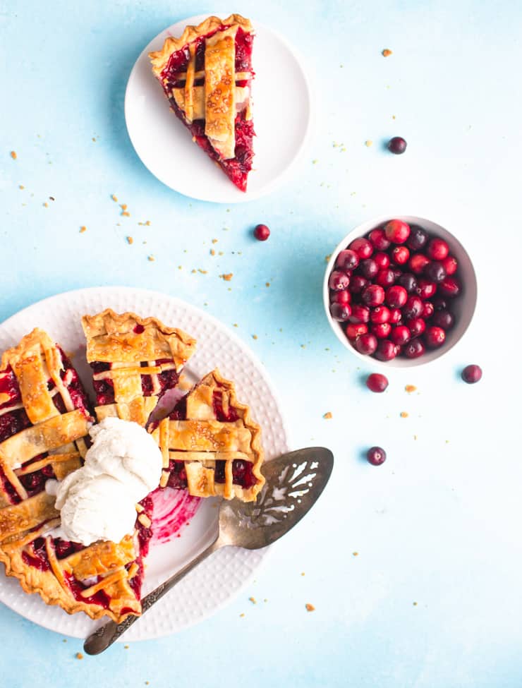 slice pie on a plate with two scoops of ice cream next to a plated slice of pie and a bowl of cranberries