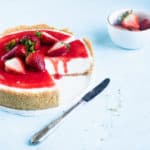 sliced cheesecake with strawberries on top and a strawberry drip down the sliced side