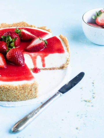 sliced cheesecake with strawberries on top and a strawberry drip down the sliced side