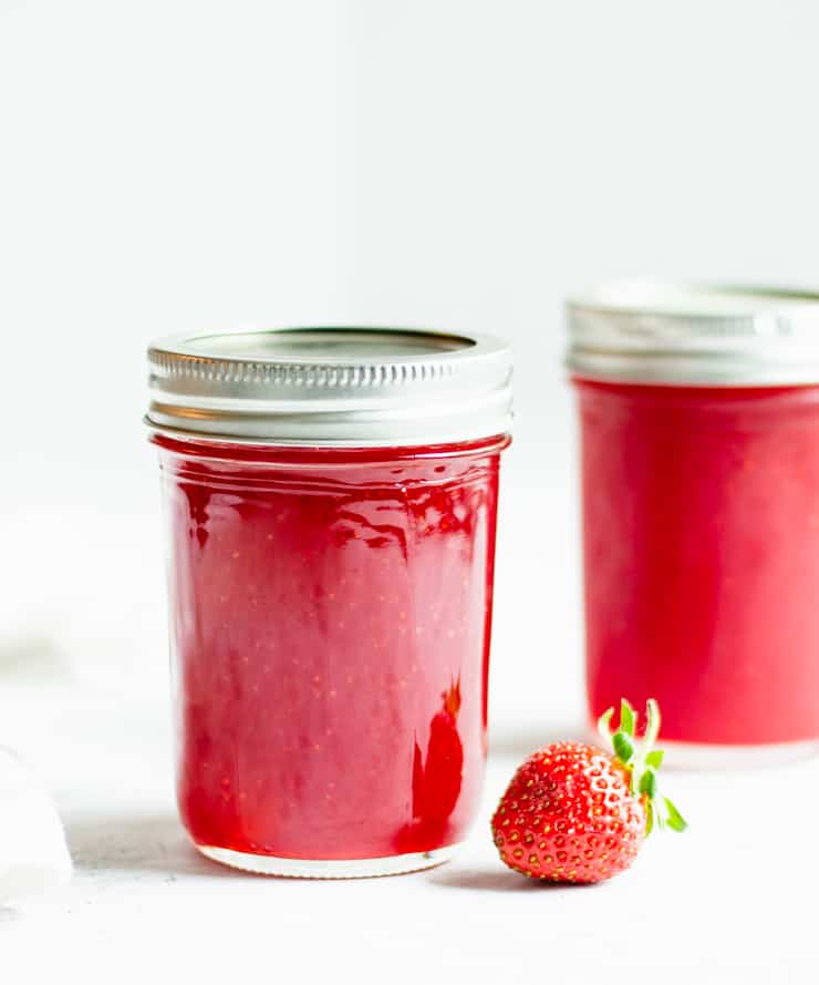 two jars of strawberry jam with a strawberry in front