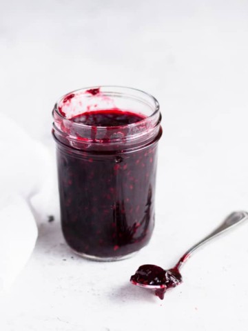 jar of blackberry cherry jam with a spoon of jam next to it