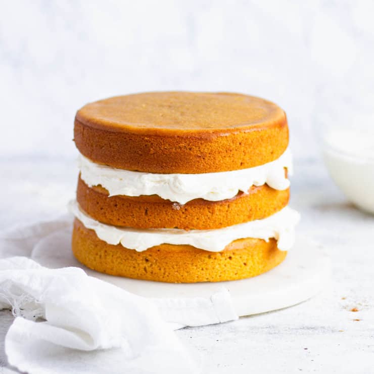 Layers of orange sweet potato cake filled with frosting next to a clear bowl of white frosting.