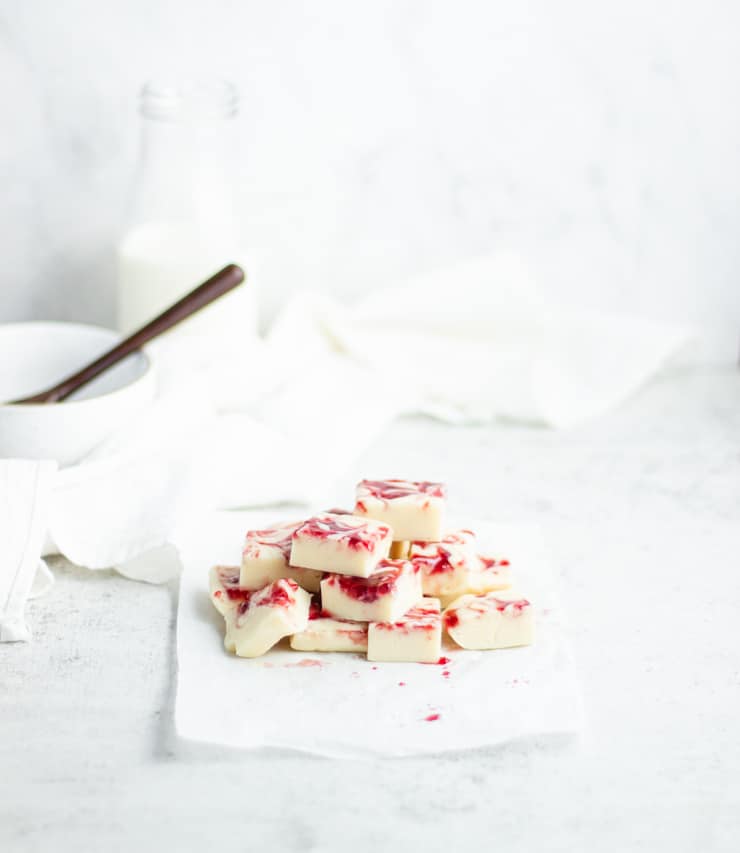 pile of white chocolate fudge with raspberry swirl with a bowl and glass of milk in the background
