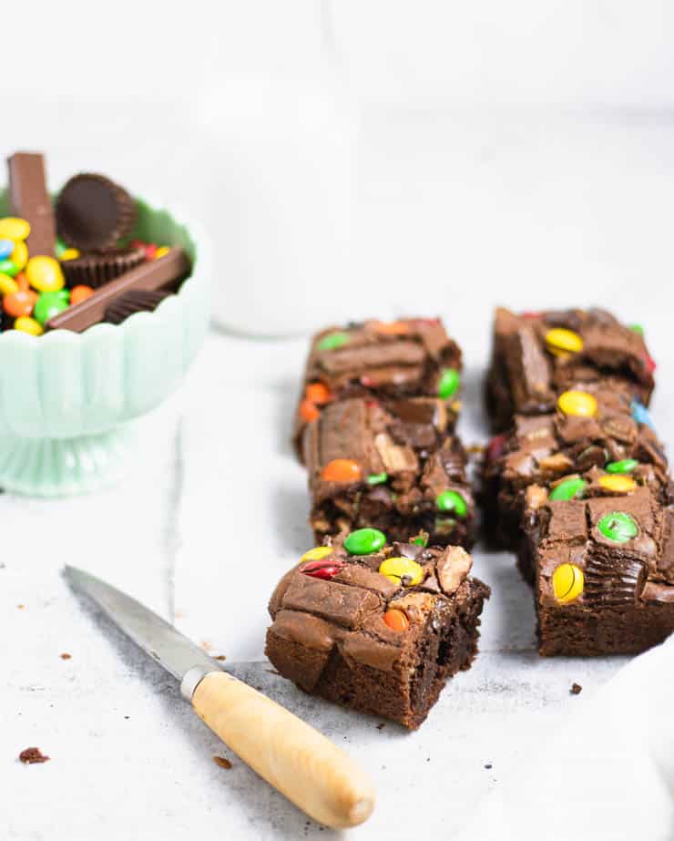 brownies with candy pieces on top next to a bowl of candy and a glass of milk