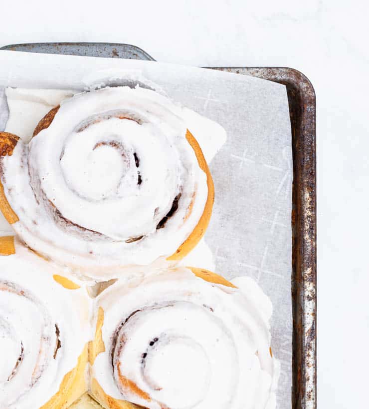 overhead view of iced cinnamon rolls on a parchment paper lined baking sheet