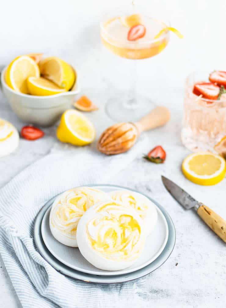 lemon meringue cookies on a plate with drinks and fresh fruit in the background