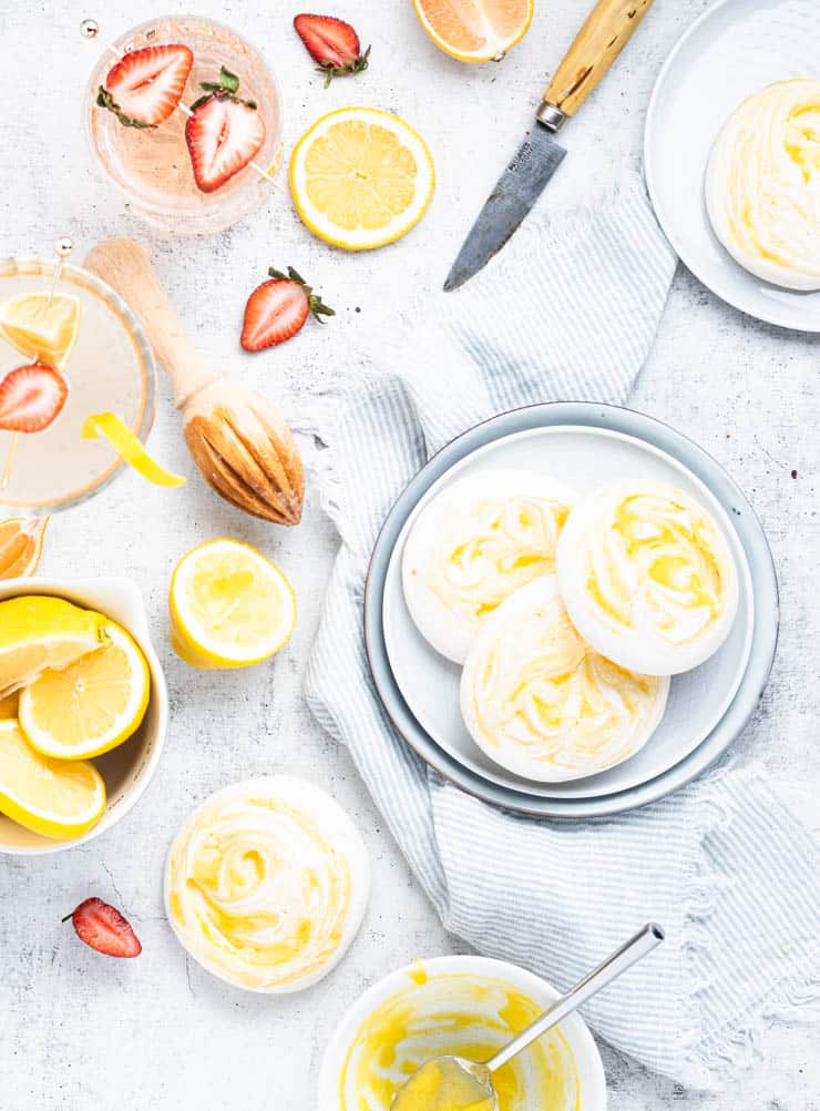 overhead view of meringue cookies on plates with strawberries and lemons around them