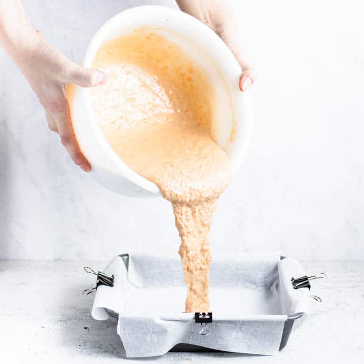 side view of carrot cake batter being poured into a parchment paper lined cake pan