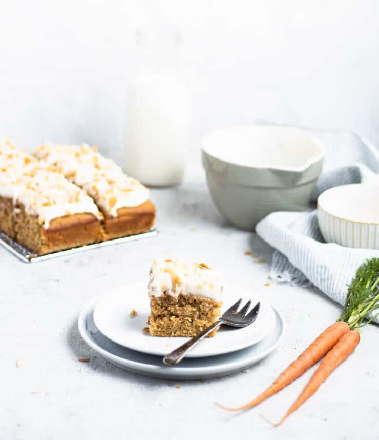 slice of carrot cake on a plate with mini sheet cake in the background