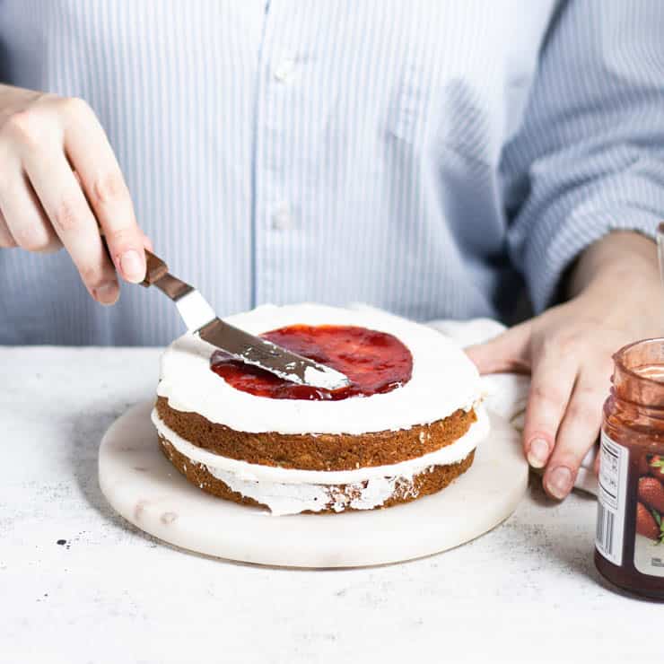 jam being spread in the center of a layer of cake