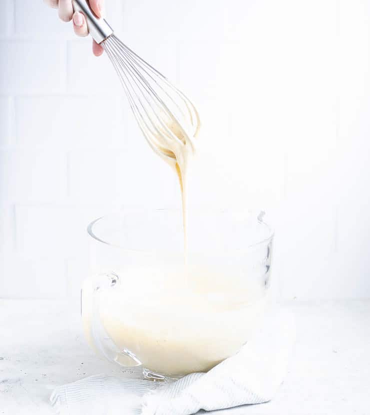 cake batter dripping off of a whisk back into a large, clear bowl.