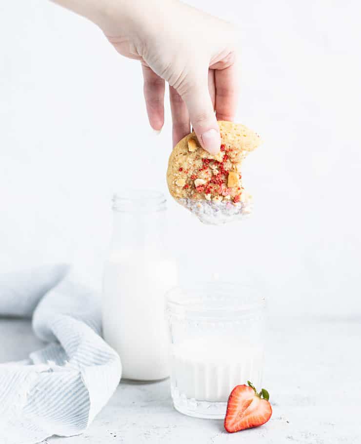 hand dipping strawberry cookie into a glass of milk.