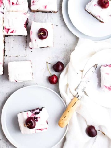 overhead view of sliced cheesecake on plates topped with cherries.