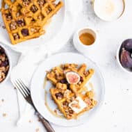 two triangles of waffles on a blue plate topped with a square of butter, a halved fig and granola.