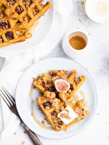 two triangles of waffles on a blue plate topped with a square of butter, a halved fig and granola.