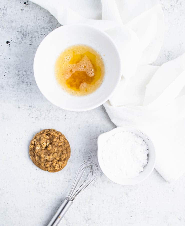 a baked pumpkin oatmeal cookie next to a bowl of browned butter and powdered sugar.