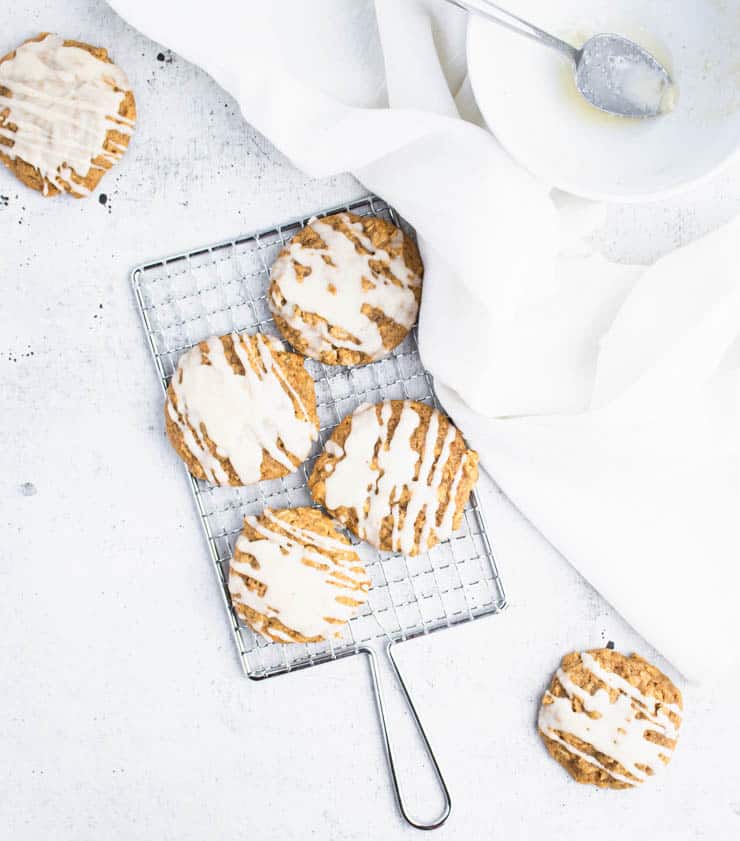 brown butter iced pumpkin cookies on a small silver cooling rack next to a piece of white linen and a bowl.
