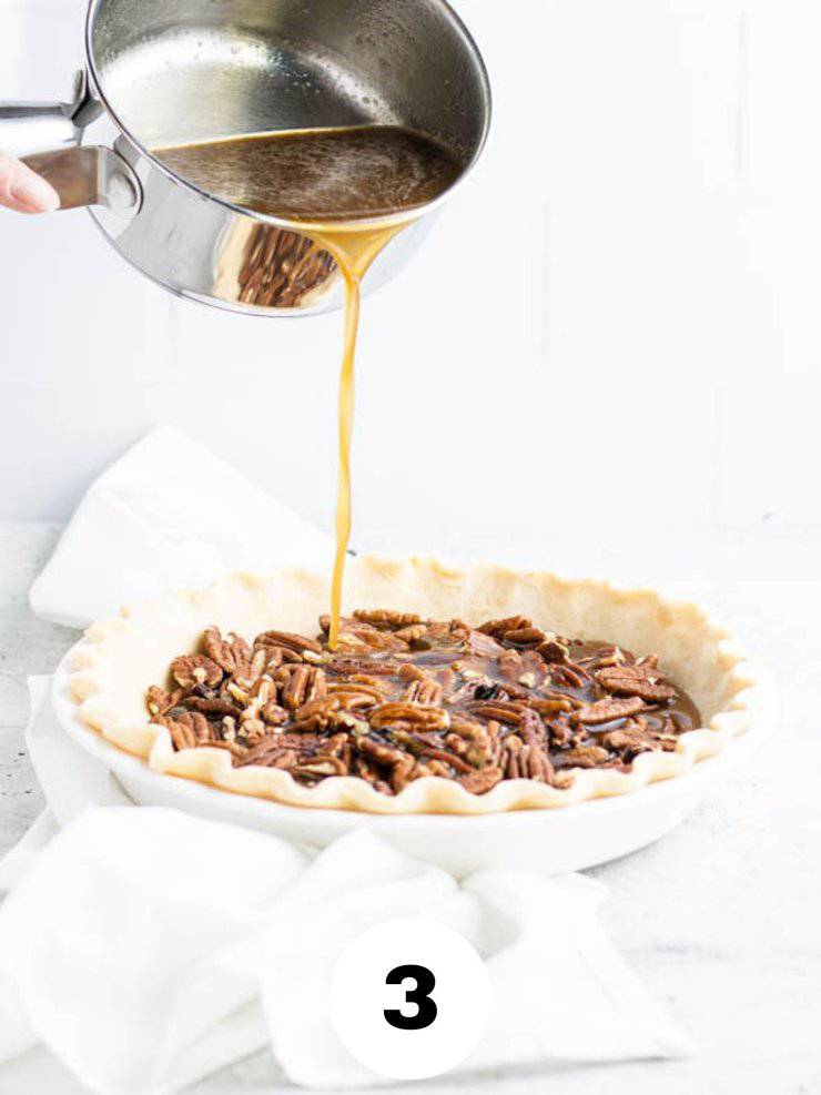 hot syrup mixture being poured from a small silver saucepan into a pie crust with pecans.