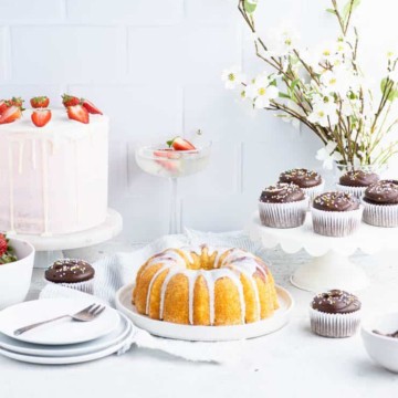 a selection of layer cakes, bundt cakes and cupcakes in front of a white tile backdrop