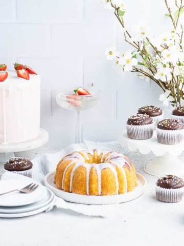 a selection of layer cakes, bundt cakes and cupcakes in front of a white tile backdrop