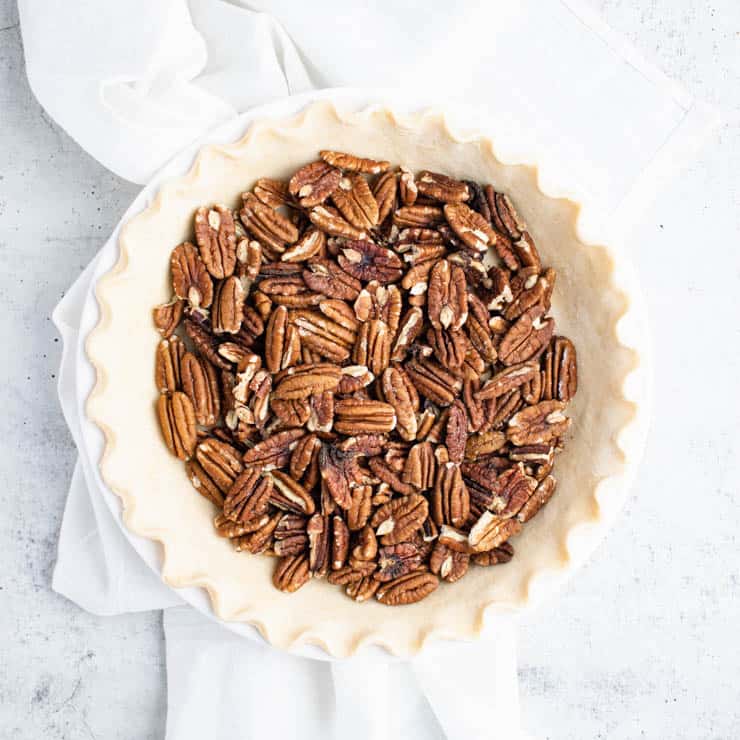 pie crust in a white pie pan filled with halved pecans.
