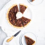 baked bourbon pecan pie sliced with a scoop of praline ice cream on top and two plated slices around it.