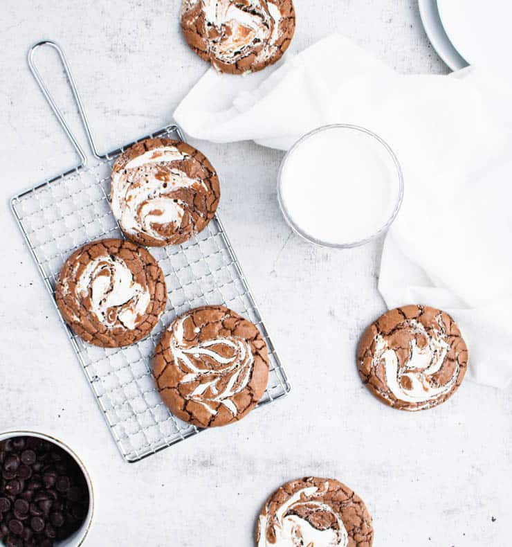 Overhead view of hot chocolate cookies on a cooling rack with a bowl of chocolate and a glass of milk arranged around it.
