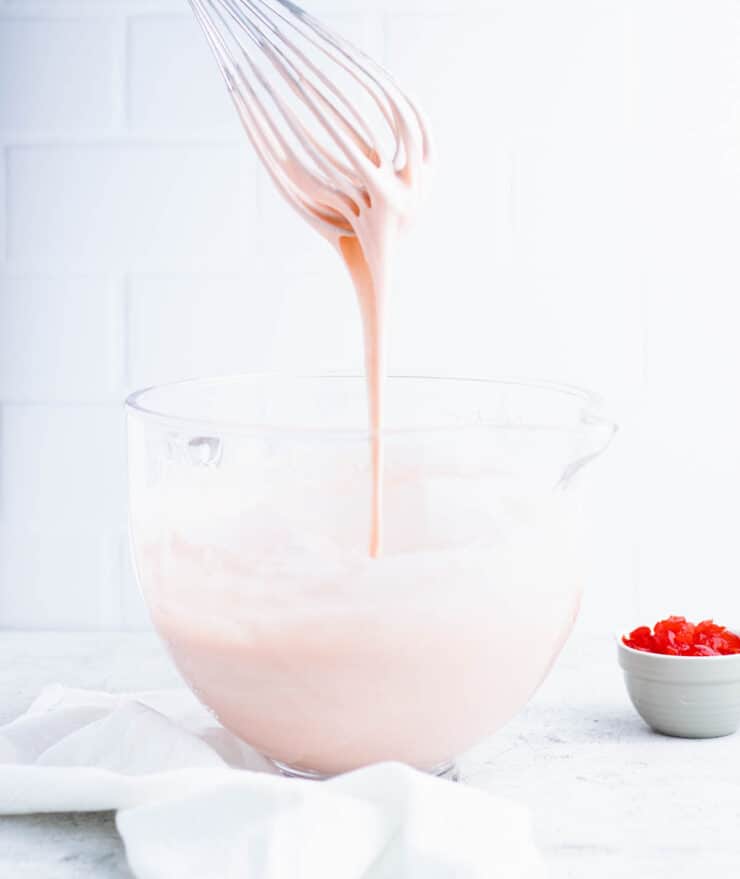 Side view of pink cake batter dripping off of a whisk to show batter consistency.
