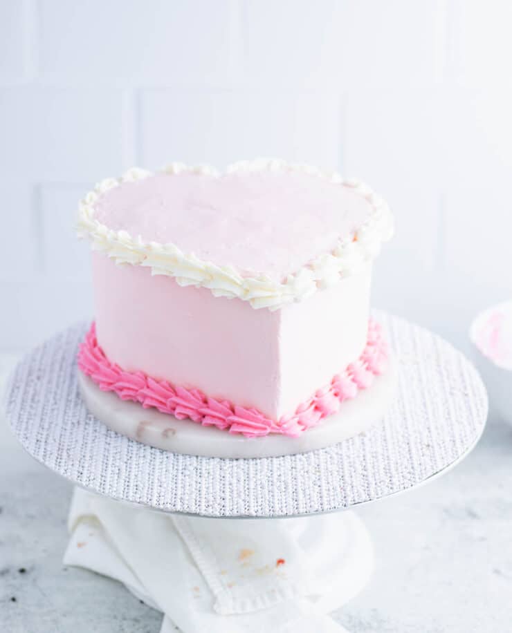 Side view of pink heart cake with a shell border on the top and bottom of the sides.
