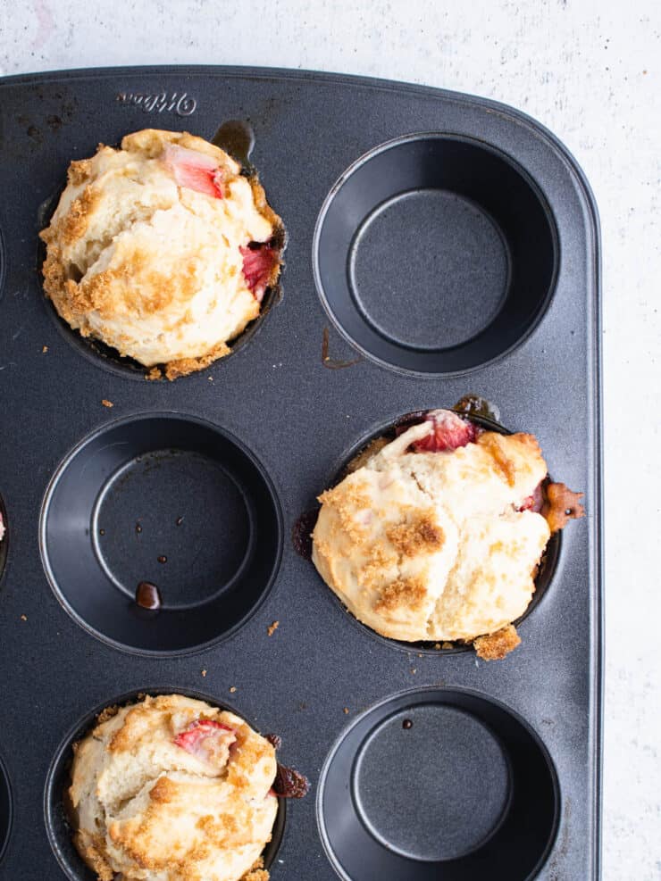 Baked strawberry muffins in a dark muffin pan.