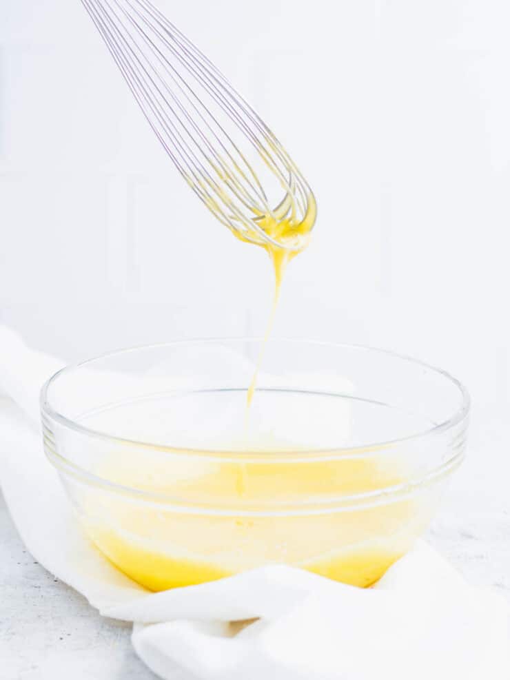 Cooked lemon curd dripping off a whisk into a clear bowl.