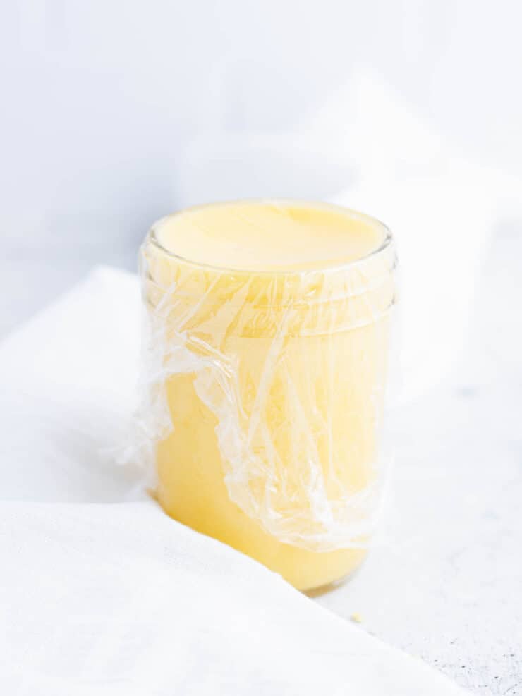 Jar of lemon curd with a piece of plastic wrap over it.