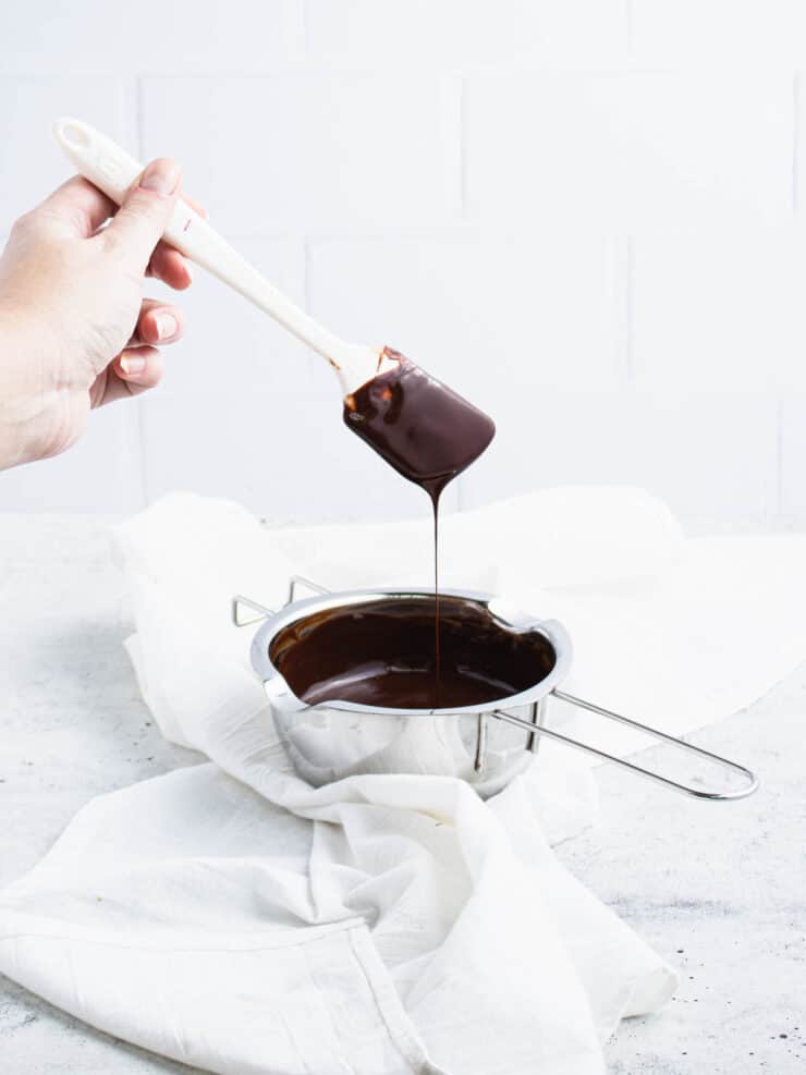 Chocolate and butter dripping off a spatula back into a silver bowl.