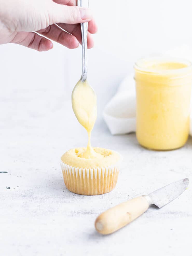Cupcake with lemon curd dripping from a spoon into a whole in the center of the cupcake.