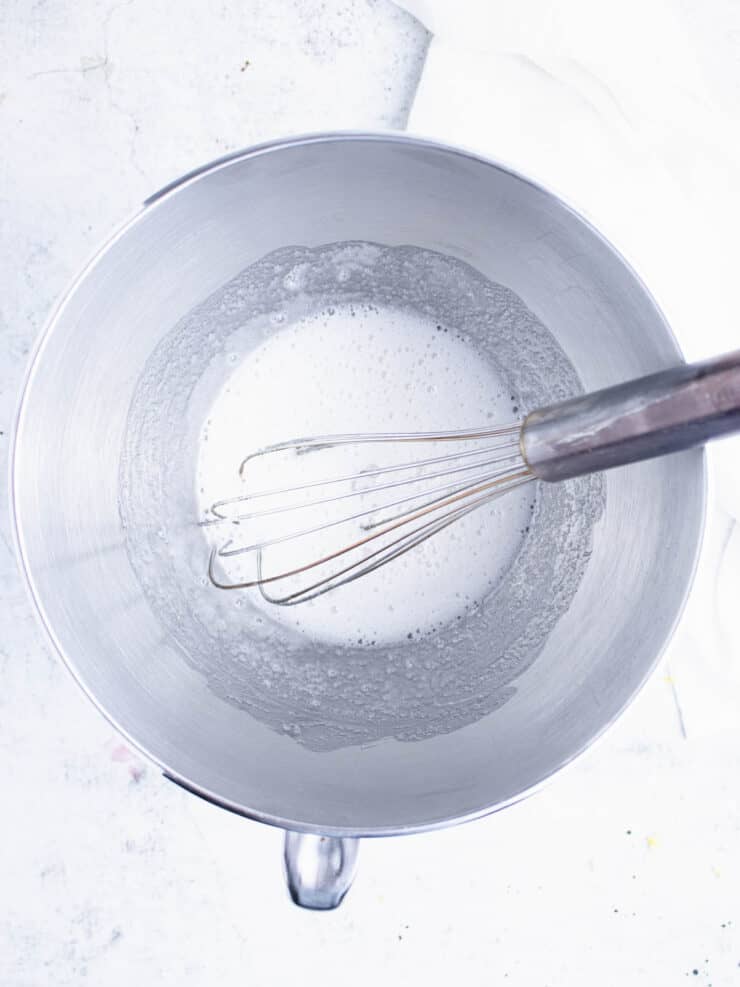 Egg whites and sugar whisked together in a silver stand mixer bowl.
