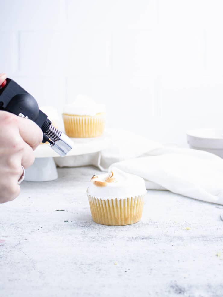 A chef's torch toasting the meringue frosting on top of a lemon cupcake.